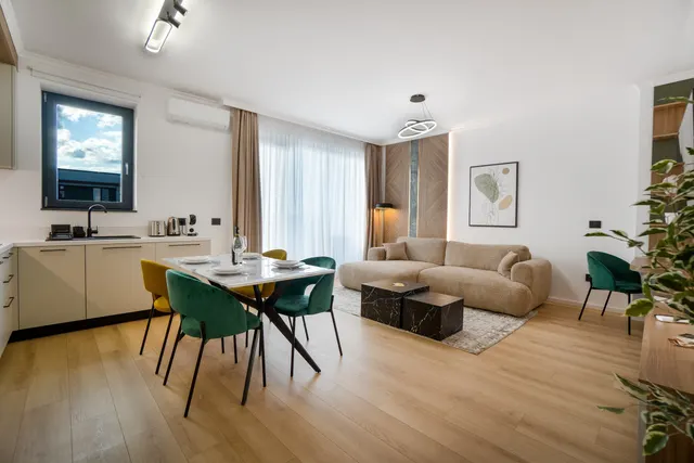 Living deschis cu canapea bej, masă cu scaune verzi și bucătărie, la Coresi, Brașov